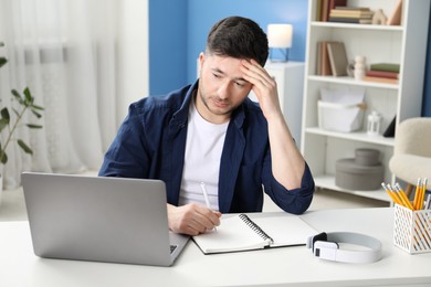 Photo of Man taking notes during online lesson at desk indoors. Self-study