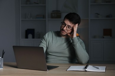 Photo of Man learning online using laptop at desk indoors in evening. Self-study