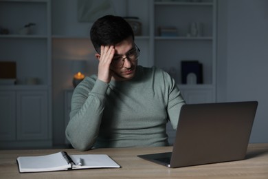 Photo of Man learning online using laptop at desk indoors in evening. Self-study