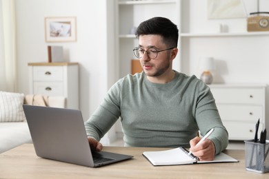 Photo of Man taking notes during online lesson at desk indoors. Self-study