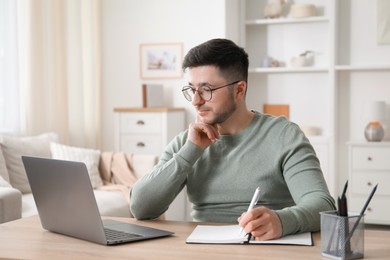 Photo of Man taking notes during online lesson at desk indoors. Self-study