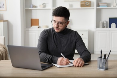 Photo of Man taking notes during online lesson at desk indoors. Self-study