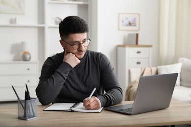 Photo of Man taking notes during online lesson at desk indoors. Self-study