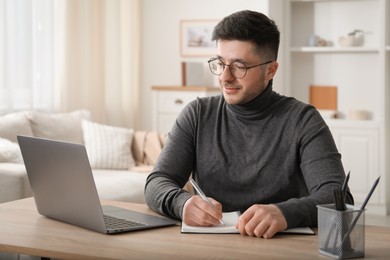 Photo of Man taking notes during online lesson at desk indoors. Self-study