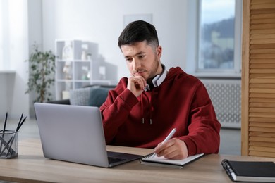 Photo of Man taking notes during online lesson at desk indoors. Self-study