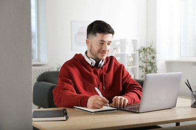 Photo of Man taking notes during online lesson at desk indoors. Self-study