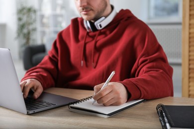 Photo of Man taking notes during online lesson at desk indoors, closeup. Self-study