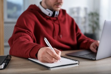 Photo of Man taking notes during online lesson at desk indoors, closeup. Self-study