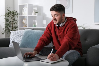 Photo of Man taking notes during online lesson at table indoors. Self-study