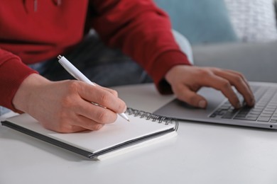 Photo of Man taking notes during online lesson at table indoors, closeup. Self-study