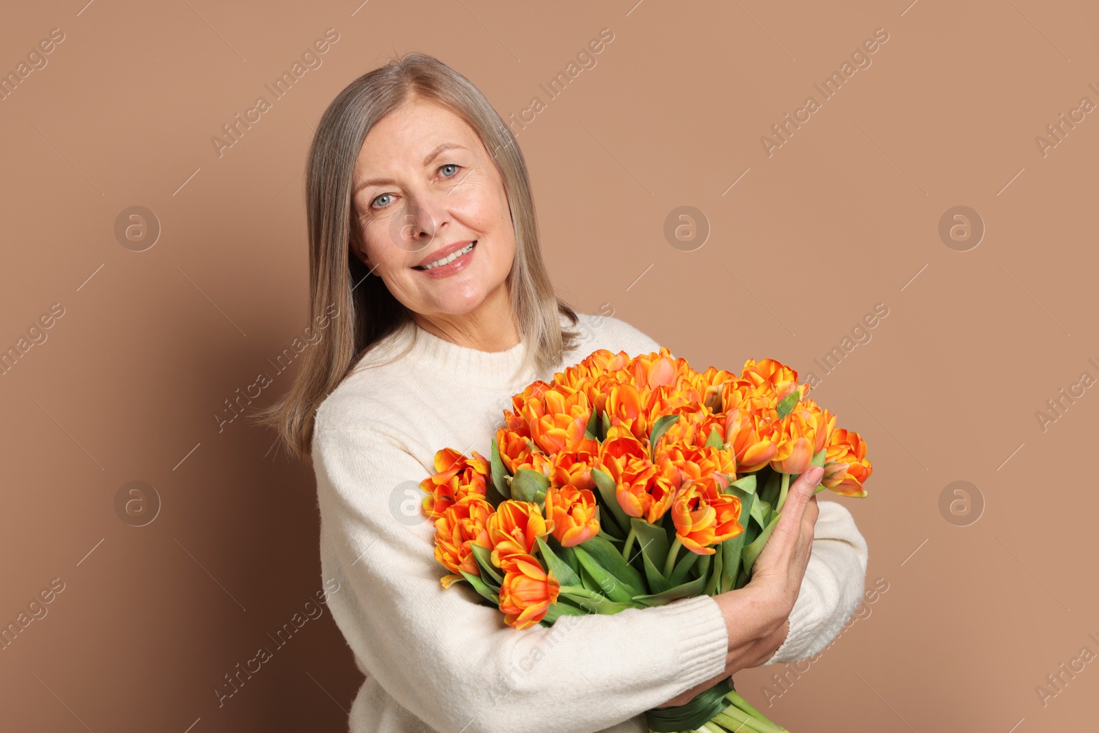 Photo of Smiling woman with bouquet of tulips on beige background