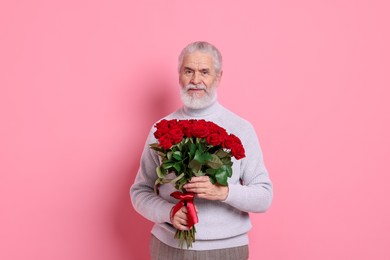 Photo of Senior man with bouquet of red roses on pink background