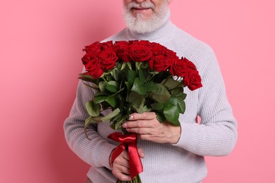 Photo of Senior man with bouquet of red roses on pink background, closeup