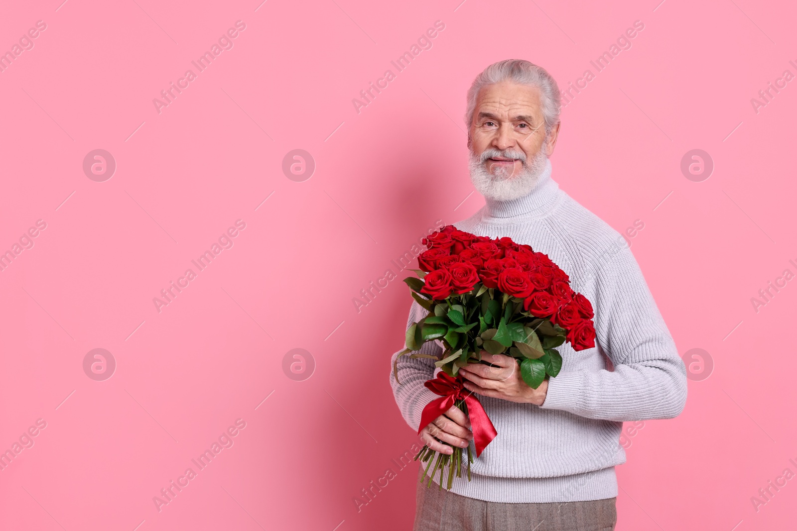 Photo of Senior man with bouquet of red roses on pink background, space for text