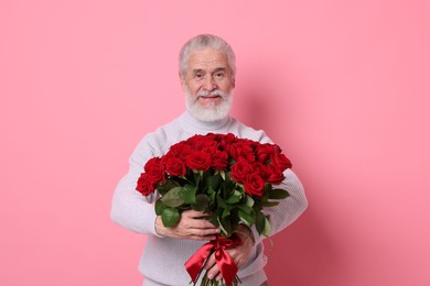 Photo of Senior man with bouquet of red roses on pink background