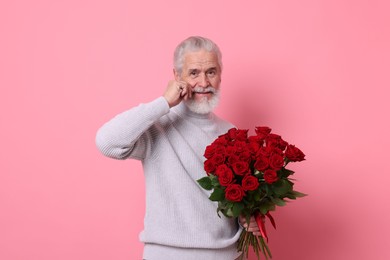 Photo of Senior man with bouquet of red roses on pink background