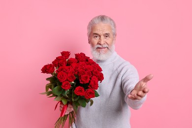 Photo of Senior man with bouquet of red roses on pink background