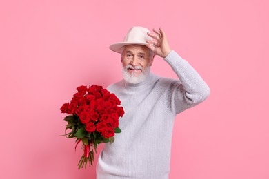 Photo of Senior man with bouquet of red roses on pink background