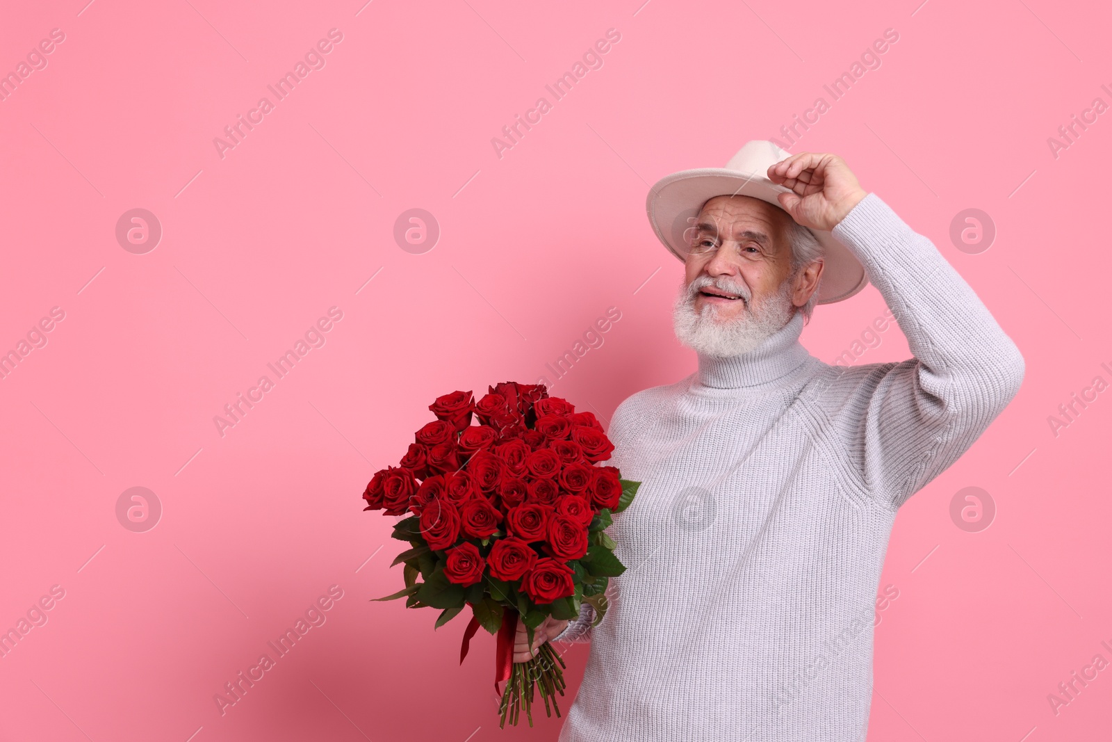 Photo of Senior man with bouquet of red roses on pink background, space for text