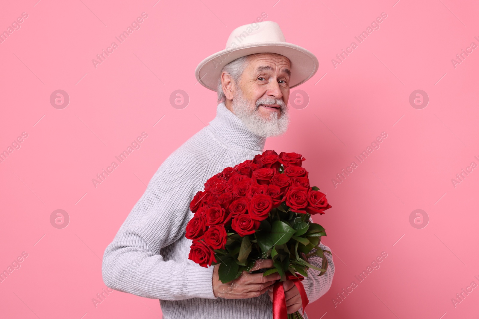 Photo of Senior man with bouquet of red roses on pink background