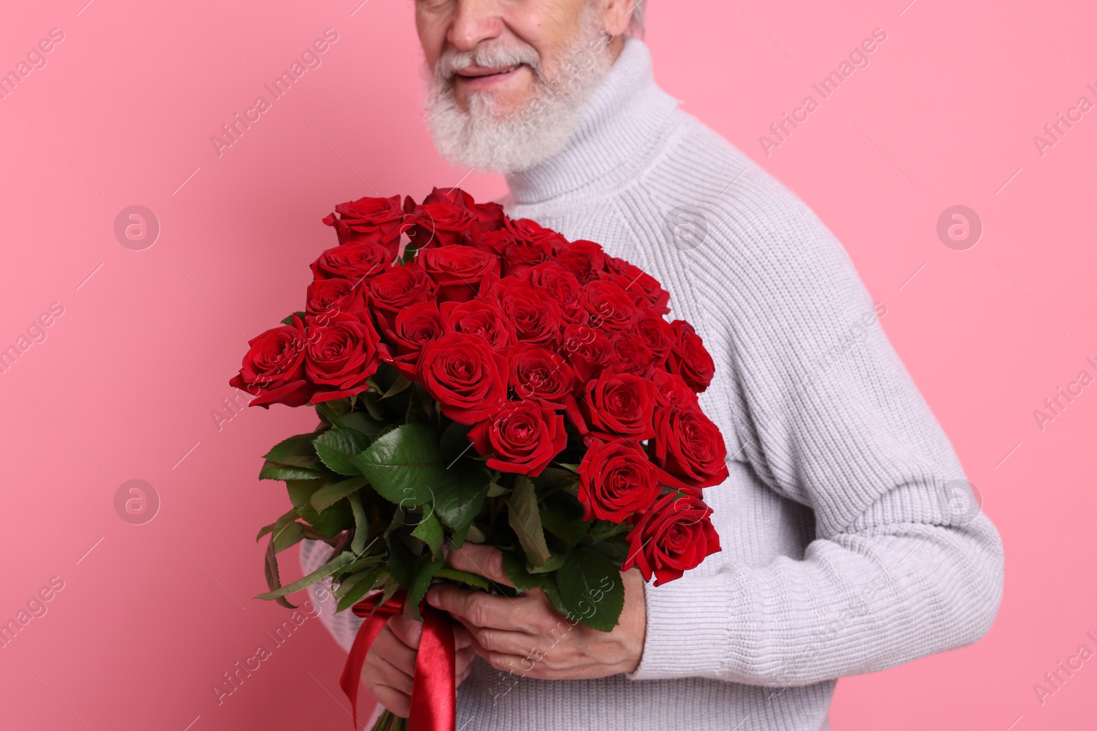 Photo of Senior man with bouquet of red roses on pink background, closeup