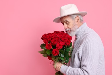 Photo of Senior man with bouquet of red roses on pink background, space for text