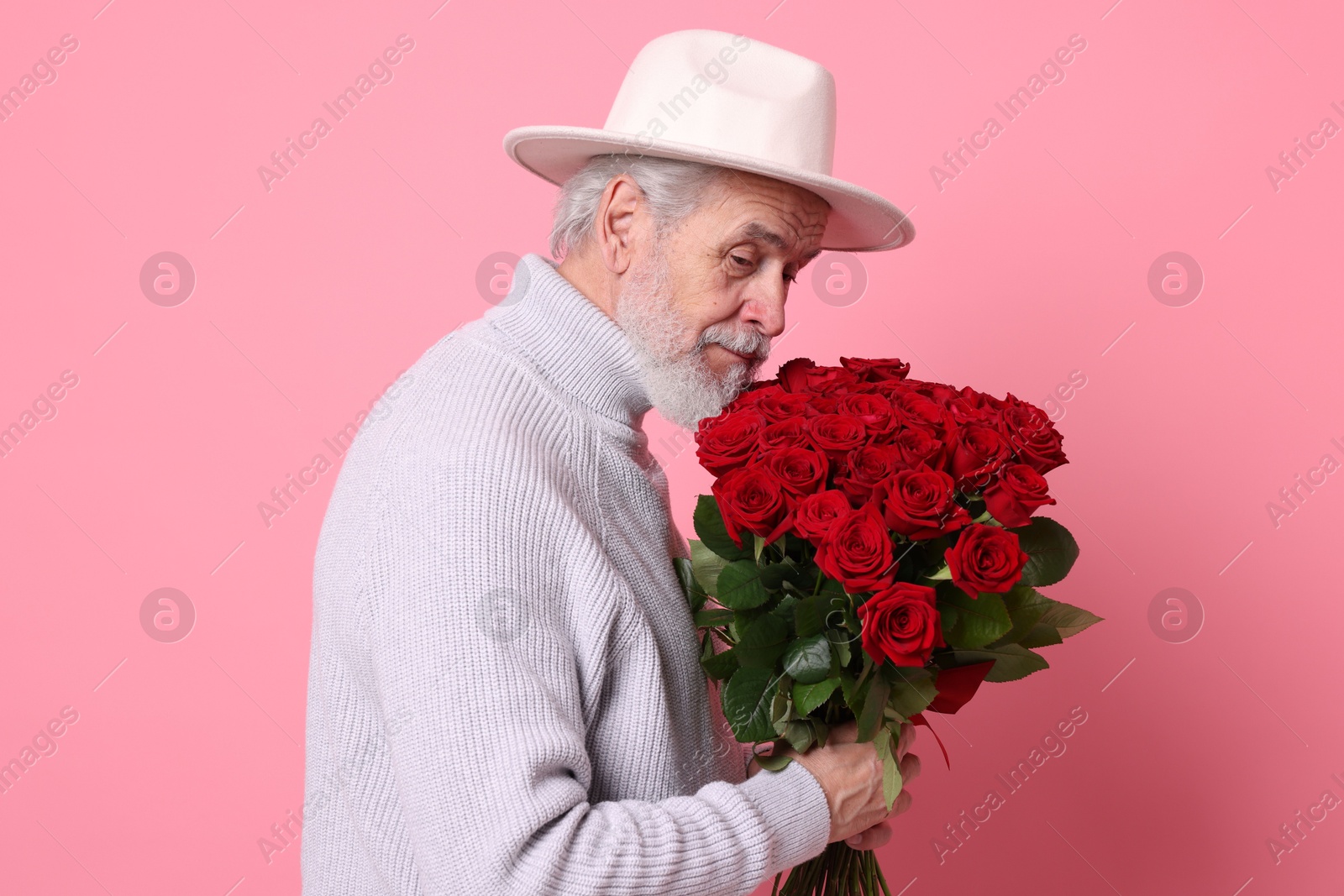 Photo of Senior man with bouquet of red roses on pink background