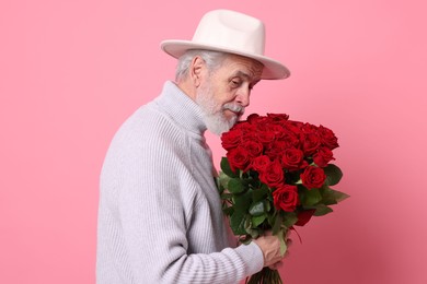 Photo of Senior man with bouquet of red roses on pink background