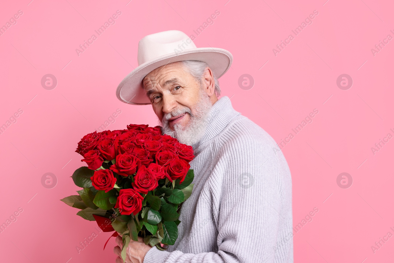 Photo of Senior man with bouquet of red roses on pink background