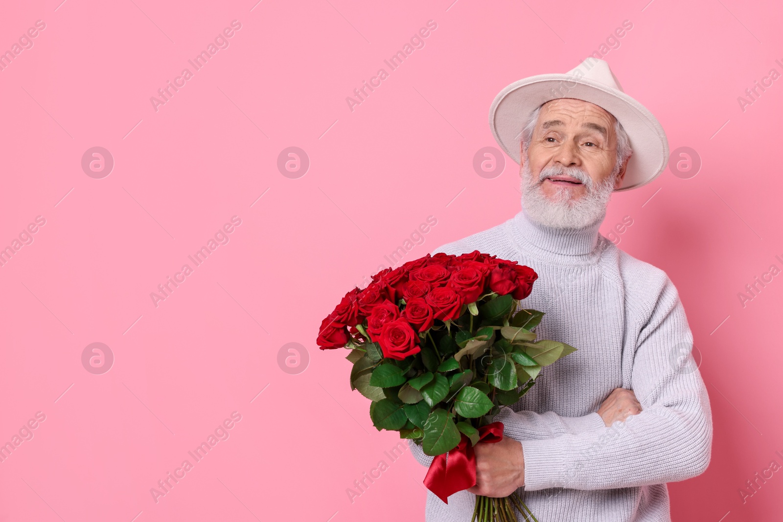 Photo of Senior man with bouquet of red roses on pink background, space for text