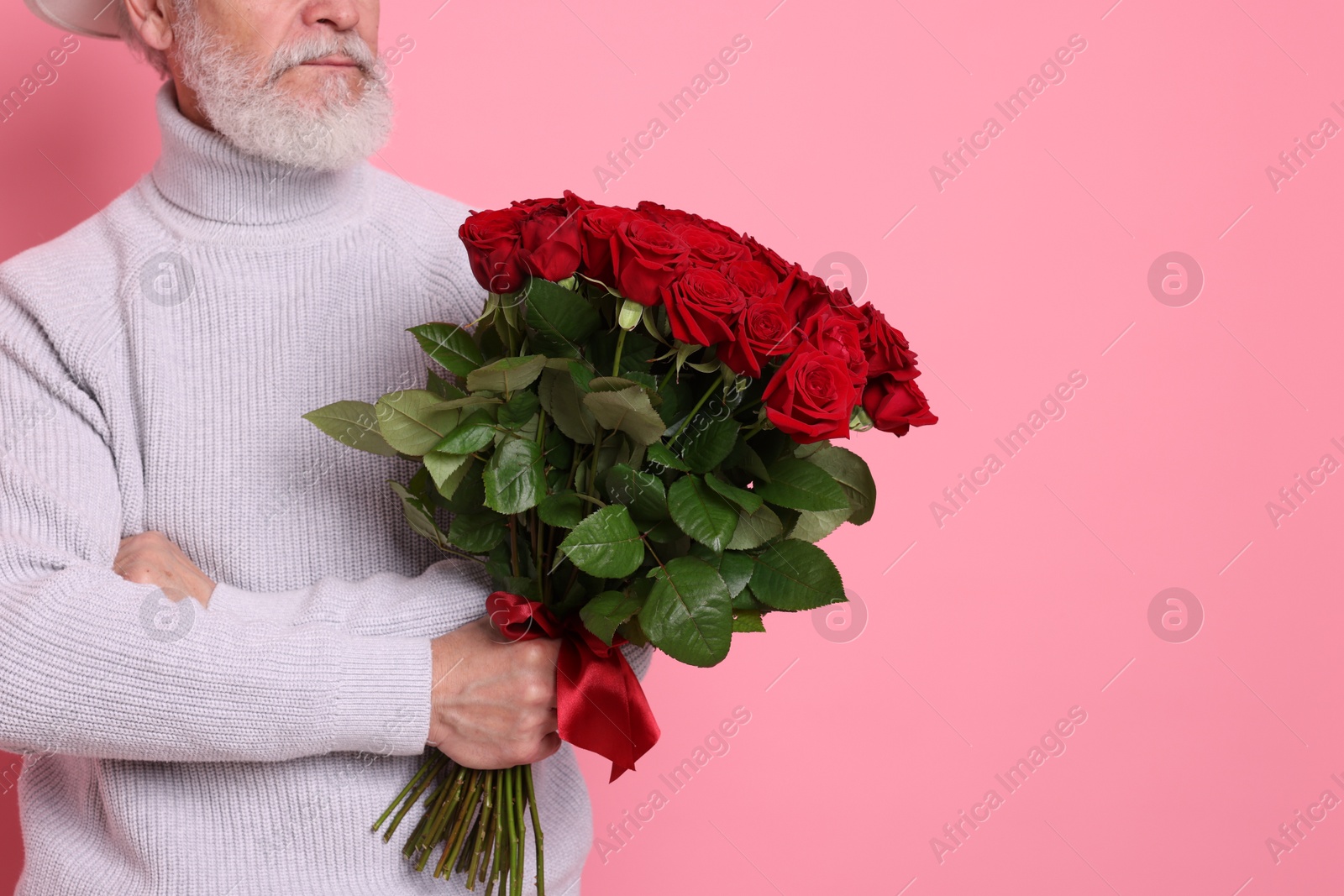 Photo of Senior man with bouquet of red roses on pink background, closeup. Space for text