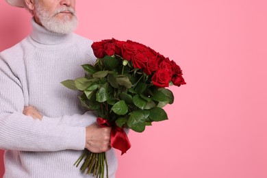 Photo of Senior man with bouquet of red roses on pink background, closeup. Space for text