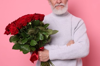 Photo of Senior man with bouquet of red roses on pink background, closeup