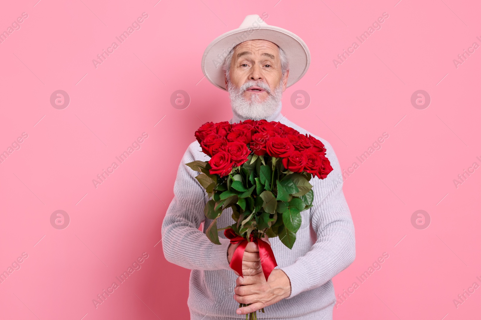 Photo of Senior man with bouquet of red roses on pink background