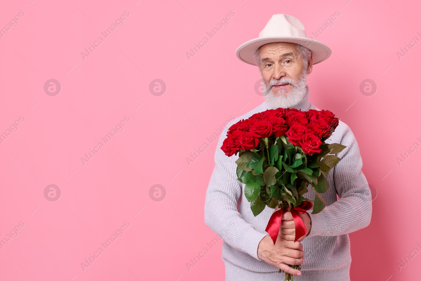 Photo of Senior man with bouquet of red roses on pink background, space for text