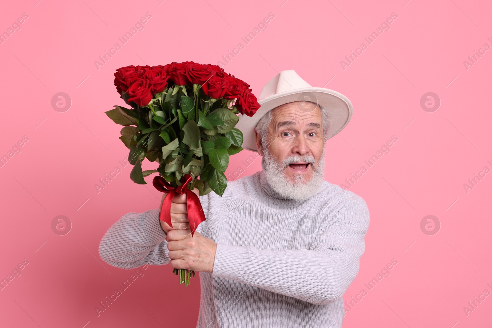 Photo of Senior man with bouquet of red roses on pink background