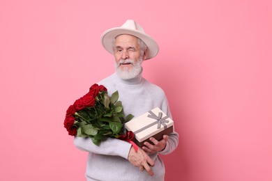 Photo of Senior man with bouquet of red roses and gift box on pink background