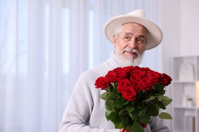 Photo of Senior man with bouquet of red roses at home, space for text