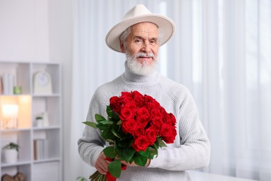 Photo of Senior man with bouquet of red roses at home