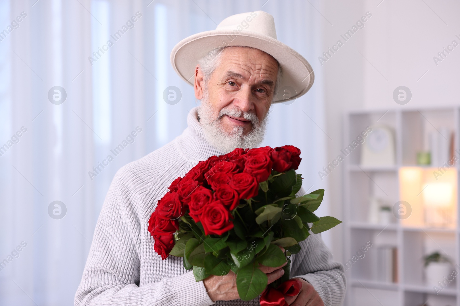 Photo of Senior man with bouquet of red roses at home