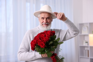 Photo of Senior man with bouquet of red roses at home