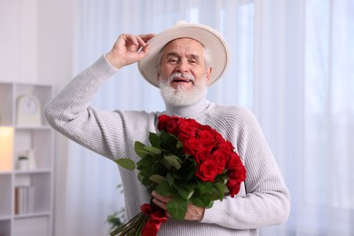 Photo of Senior man with bouquet of red roses at home