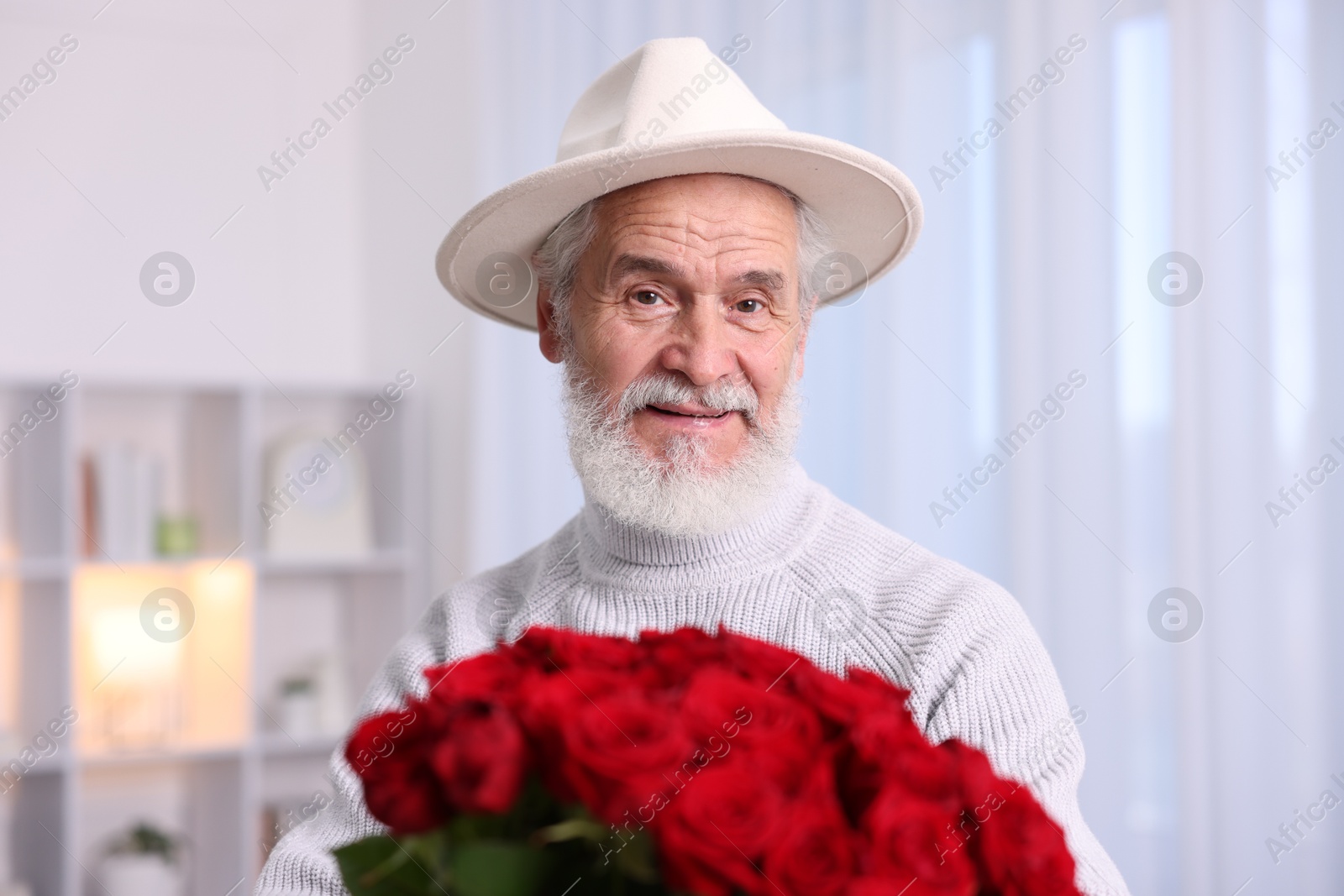 Photo of Senior man with bouquet of red roses at home