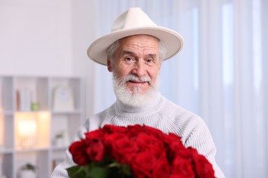 Photo of Senior man with bouquet of red roses at home