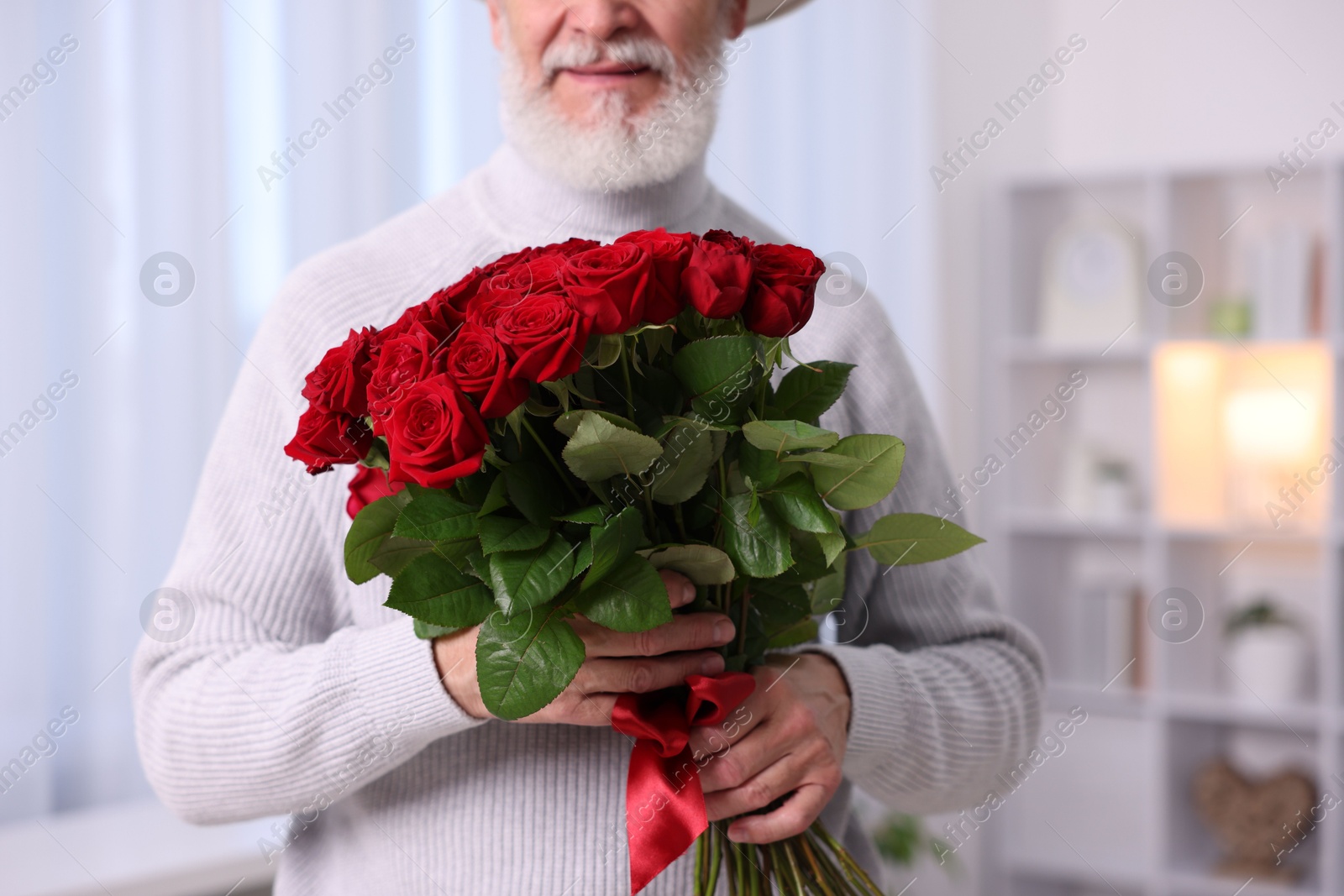 Photo of Senior man with bouquet of red roses at home, closeup