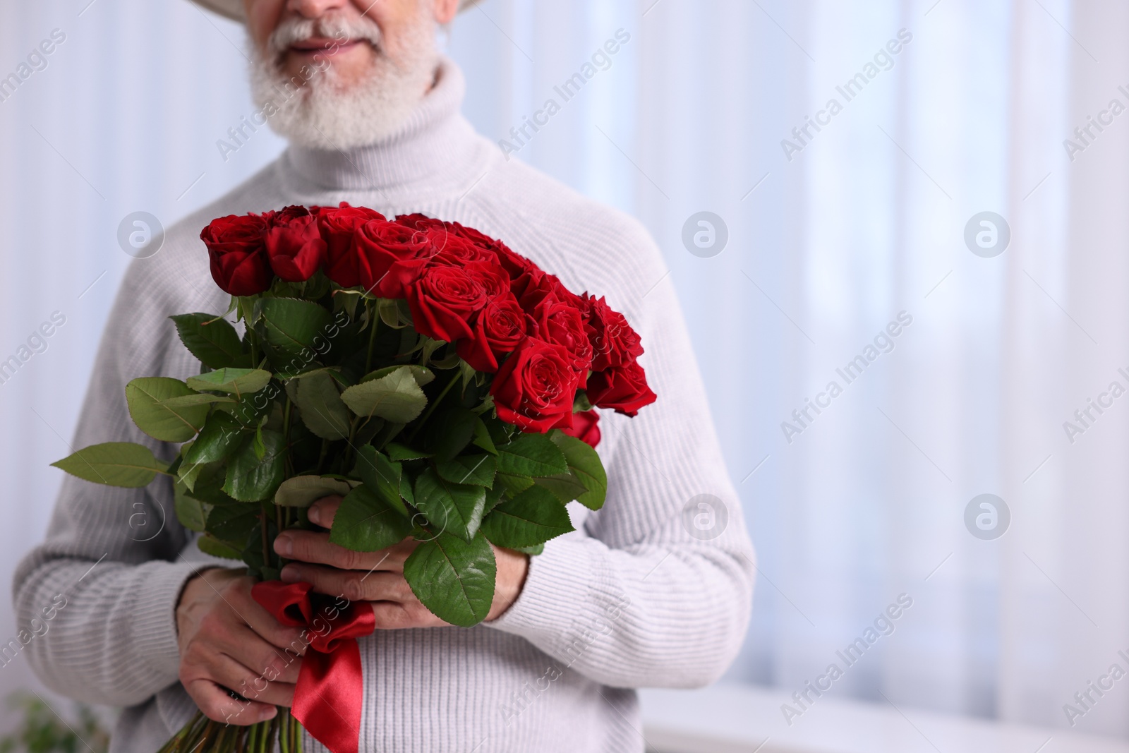 Photo of Senior man with bouquet of red roses at home, closeup. Space for text