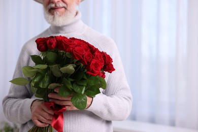 Photo of Senior man with bouquet of red roses at home, closeup. Space for text