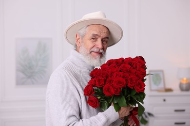 Photo of Senior man with bouquet of red roses at home