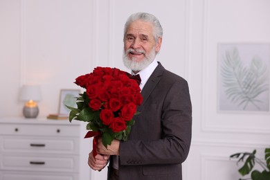 Photo of Senior man with bouquet of red roses at home