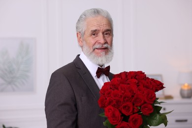 Photo of Senior man with bouquet of red roses at home